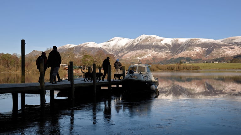 Visitors with their dogs walking along a pier to board a boat on a sunny winter's day